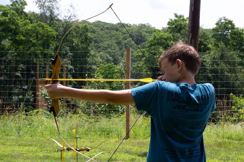 A person practicing archery outdoors, aiming with a bow and arrow.