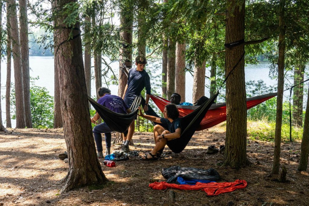 People relaxing in hammocks among trees by a lake.