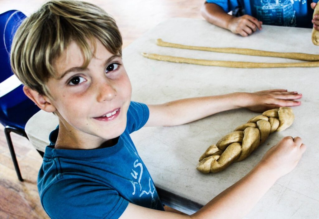 A child smiling while crafting a braided dough on a table.