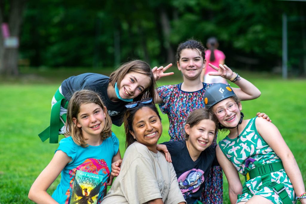 Group of children and a counselor smiling outside on a grassy field.