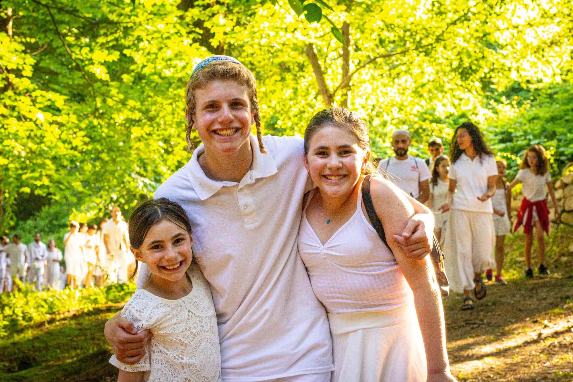 People smiling outdoors in sunlit forest, enjoying a gathering.