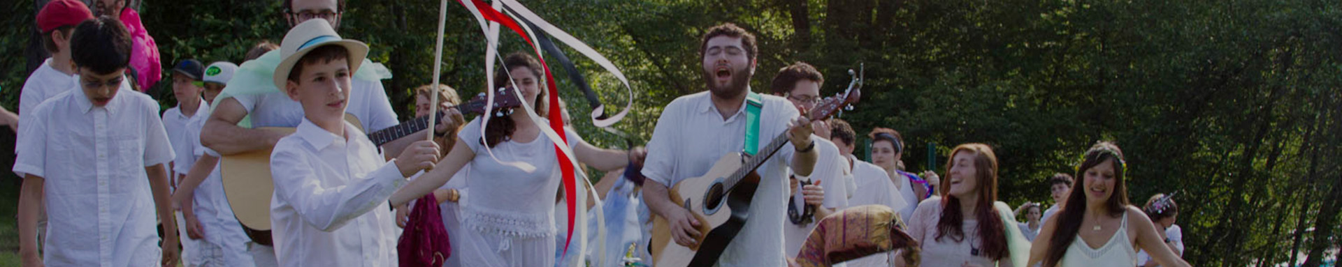 A joyful gathering of individuals in white, celebrating outdoors with music and ribbons.